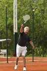 Giocatore di tennis senior attivo che serve palla sul campo . — Foto stock