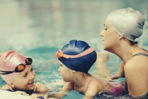 Female instructor having with kids swimming lesson in swimming pool. — Stock Photo