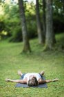 Mulher fazendo ioga no tapete no parque, meditando na posição shavasana . — Fotografia de Stock