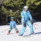 Kleiner Junge in Winterkleidung lernt mit Vater Skifahren im verschneiten Skigebiet. — Stockfoto