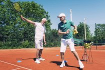 Старший мужчина, занимающийся теннисом с инструктором . — стоковое фото