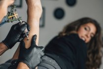 Tatuaggio artista lavorando sul tatuaggio della gamba femminile
. — Foto stock