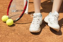 Feet of female tennis player on break with tennis shoes, racket and balls. — Stock Photo