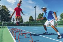 Adolescent tennis player jumping with male instructor in tennis class. — Stock Photo