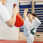 Chica pateando saco de boxeo en clase taekwondo con entrenador . - foto de stock