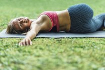 Giovane donna che fa yoga, pratica reclinabile torsione spinale posizione sul tappeto nel parco . — Foto stock