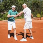 Istruttore di tennis che lavora con l'uomo anziano e che pratica la posizione per il colpo frontale . — Foto stock
