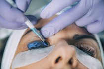 Косметолог ставить синю фарбу на вії пацієнта під час підйому і ламінування вій. — стокове фото