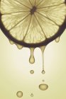 Lemon slice with drips against yellow background. — Stock Photo
