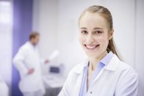 Female doctor smiling in clinic, male doctor in background. — Stock Photo