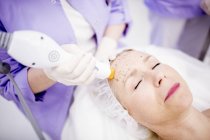 Dermatologist giving thermage treatment to mature woman forehead to softening wrinkles. — Stock Photo