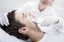 Dermatologue appliquant un traitement de microdermabrasion faciale sur l'homme en clinique, gros plan . — Photo de stock