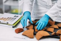 Midsection of archaeologist reconstructing broken pottery in laboratory. — Stock Photo