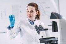 Female archaeologist looking at ancient tooth root in microscope slide in laboratory. — Stock Photo