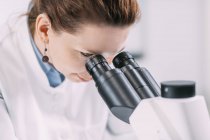 Portrait of young female archaeologist using and looking in microscope in laboratory. — Stock Photo