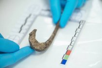 Hands of archaeologist measuring ancient hook with straightedge in archeology lab. — Stock Photo