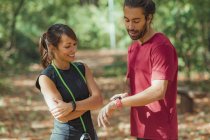 Young man checking progress on smartwatch after outdoor training with female friend. — Stock Photo