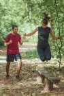 Junge Frau springt beim Training mit Personal Trainer im Park über Holzbank. — Stockfoto