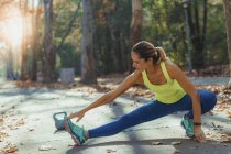 Mujer estirando las piernas como hacer ejercicio al aire libre en el parque de otoño . - foto de stock
