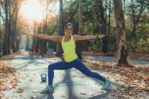 Mujer haciendo yoga y mirando en cámara, sonriendo mientras hace ejercicio al aire libre en el parque de otoño . - foto de stock