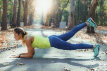 Mulher exercitando enquanto levanta as pernas na prancha ao ar livre no parque de outono . — Fotografia de Stock