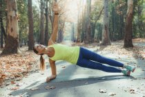 Mujer haciendo plancha lateral mientras hace ejercicio al aire libre en el parque de otoño . - foto de stock