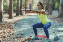 Woman squatting with resistance band outdoors in autumn park. — Stock Photo