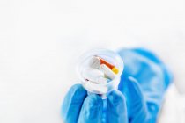 Medico donna mano in guanto blu tenendo graduato medicina tazza piena di pillole, spazio copia su sfondo bianco . — Foto stock