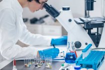 Investigador médico a examinar um novo medicamento. estudante de ciências vestida com jaleco branco olhando através de um microscópio. — Fotografia de Stock