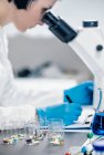 Investigador médico examinando un nuevo medicamento. estudiante de ciencias vestida con bata blanca de laboratorio mirando a través de un microscopio. - foto de stock