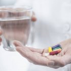 Médico mão segurando pílulas coloridas e vidro de água . — Fotografia de Stock