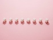 Fila de terrones de azúcar sobre fondo rosa . - foto de stock