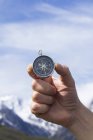 Person hält Magnetkompass gegen blauen Himmel und Berge. — Stockfoto