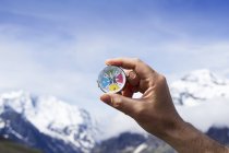 Person hand holding magnetic compass against blue sky and mountains. — Stock Photo