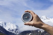Person hand holding magnetic compass against blue sky and mountains. — Stock Photo