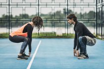 Young sporty woman crouching exercise outdoors with personal fitness trainer. — Stock Photo