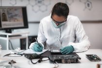 Digitale Gerichtsmedizinerin untersucht Computerfestplatte und macht sich Notizen im polizeiwissenschaftlichen Labor. — Stockfoto