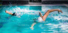 Fit women swimming together in indoor swimming pool. — Stock Photo