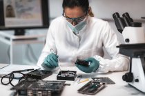 Female digital forensic expert examining computer hard drive with electronic equipment in police science laboratory. — Stock Photo
