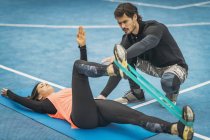 Entrenador de fitness personal que entrena a una mujer joven haciendo ejercicio de banda de resistencia en las piernas . - foto de stock