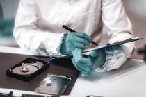 Forensic science technician taking notes while examining computer hard drive. — Stock Photo