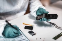 Perito forense da polícia examina telefone celular confiscado e toma notas em laboratório de ciências . — Fotografia de Stock