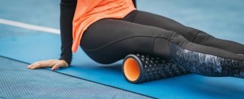 Cropped of female athlete stretching with foam roller outdoors on stadium. — Stock Photo