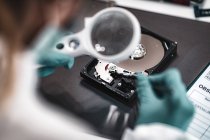 Tecnico forense digitale che esamina il disco rigido del computer con lente di ingrandimento in laboratorio . — Foto stock