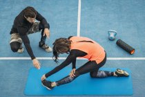 Adaptez la jeune femme faisant l'exercice d'étirement après l'entraînement avec l'entraîneur personnel de forme physique . — Photo de stock