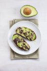 Healthy vegan snack of fresh avocado on toasts with sprouts on round plate on kitchen towel. — Stock Photo