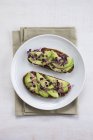 Healthy vegan snack of fresh avocado on toasts with sprouts on round plate on kitchen towel. — Stock Photo