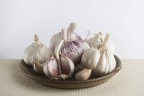 Lampadine di aglio su piatto su sfondo bianco . — Foto stock