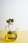 Jug of olive oil with olives on table, studio shot. — Stock Photo