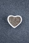 Semillas de chía negra en forma de corazón, vista superior sobre fondo gris . - foto de stock